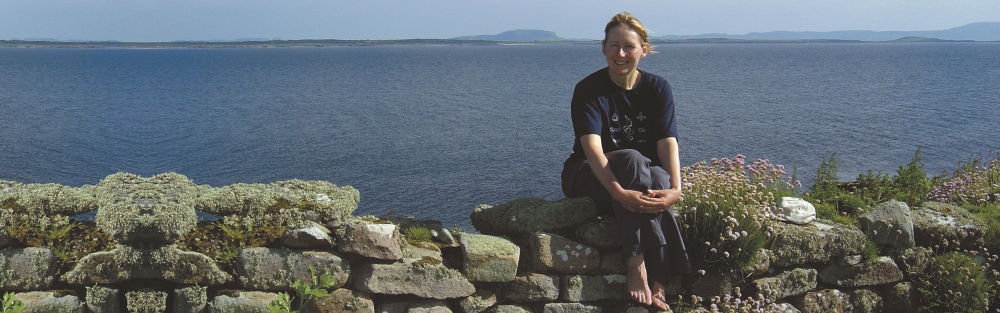 Prannie sitting on a dry stone wall with the Atlantic Ocean behind her